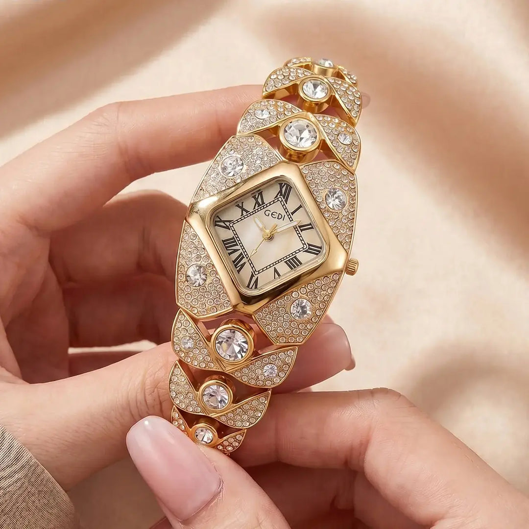 A gold-tone Tavril diamond-embellished bracelet watch with a rhombic dial featuring Roman numerals, held by a woman's hands against a soft, peachy satin background.