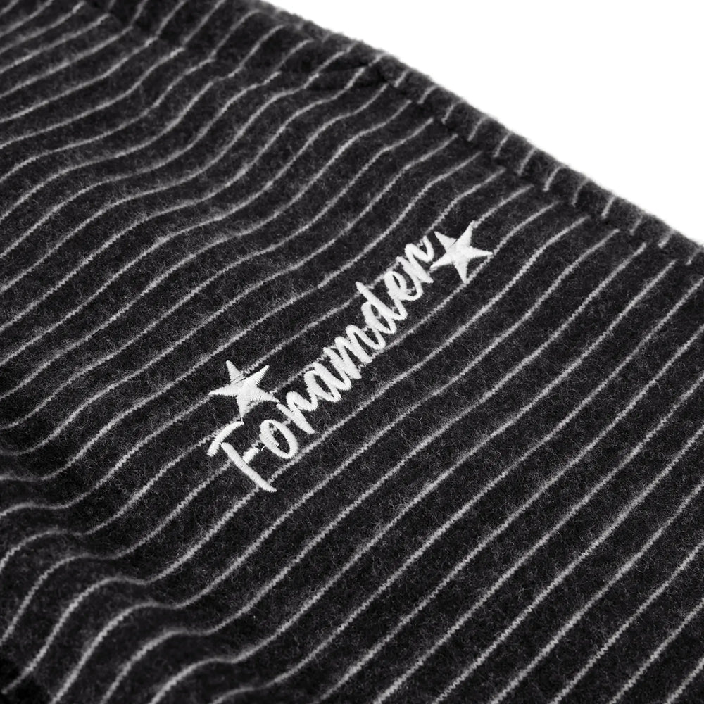 Close-up of charcoal black knit trousers featuring fine white pinstripes and a subtle embroidered logo detail with the text 'Foramnder' and stars.