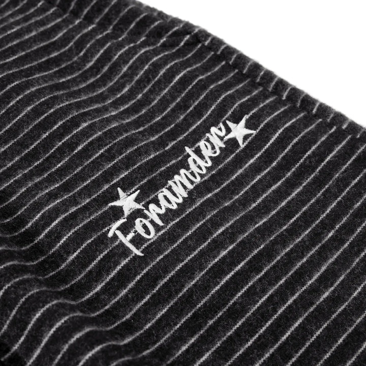 Close-up of charcoal black knit trousers featuring fine white pinstripes and a subtle embroidered logo detail with the text &
