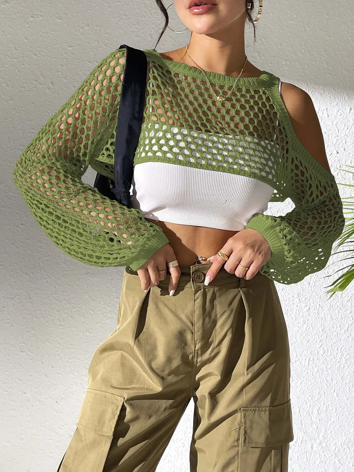 Green open-knit crochet crop top with cold-shoulder detail and voluminous long sleeves, worn by a model layered over a white tank top with khaki cargo pants.