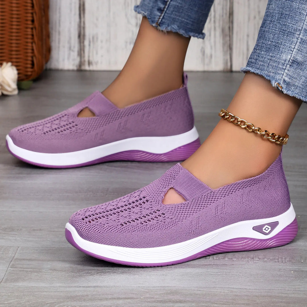 Women's Vespera breathable mesh slip-on trainers in purple, shown on a person wearing blue jeans, styled on a wooden floor.