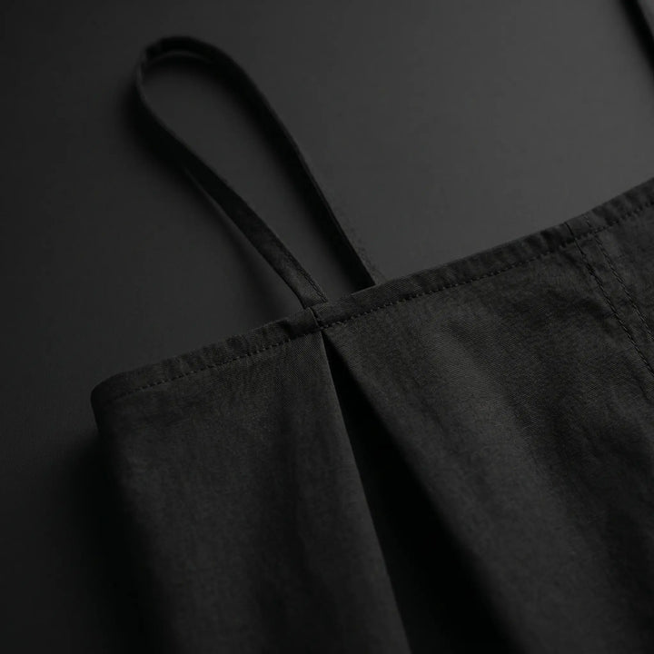 Close-up of a black Vexana cotton sling mini dress, showcasing the sharp square neckline, thin adjustable spaghetti straps, and matte fabric texture.
