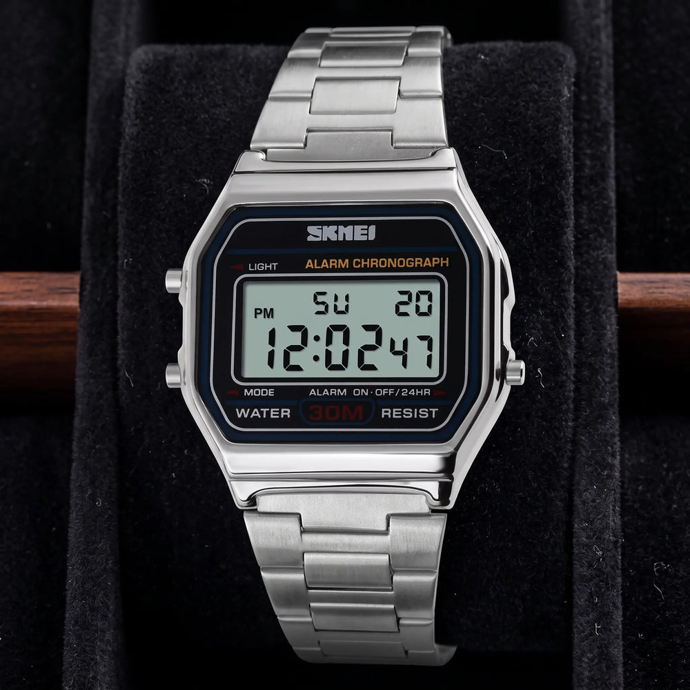 Vexil retro digital stainless steel watch in polished gold tone, front view on a white background. Features a rectangular case, link bracelet, and blue-lit LCD display showing time, date, and day.