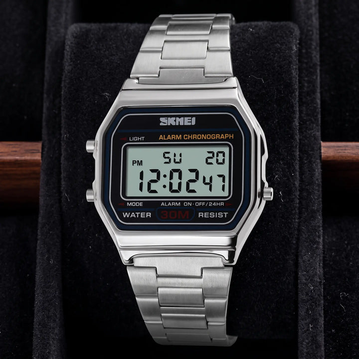 Vexil retro digital stainless steel watch in polished gold tone, front view on a white background. Features a rectangular case, link bracelet, and blue-lit LCD display showing time, date, and day.