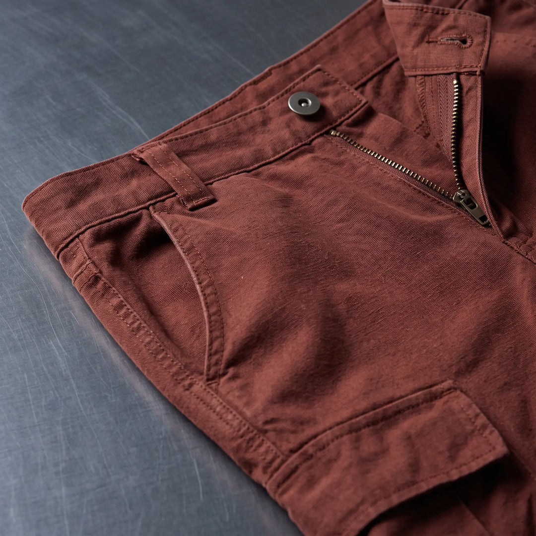 Close-up of Vextar Terracotta Rust cotton cargo pants, showing the buttoned waistband, zip fly, front pocket, and detailed flap cargo pocket construction. The durable cotton twill fabric has a matte finish.