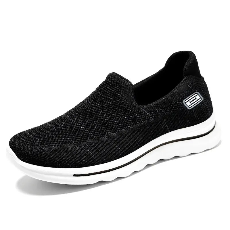 Black Veyla comfort knit slip-on trainers with a white EVA sole and a subtle textured side badge, presented from a three-quarter view.