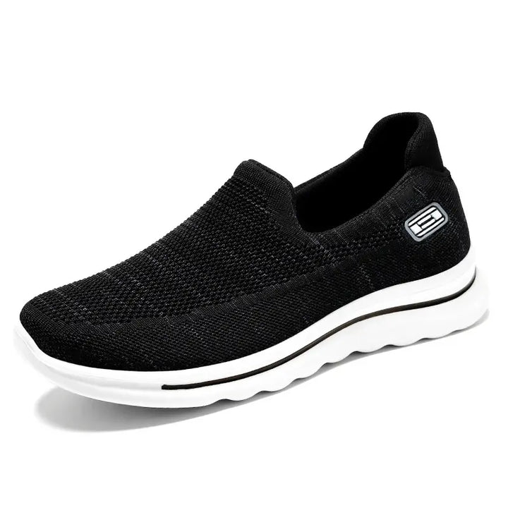 Black Veyla comfort knit slip-on trainers with a white EVA sole and a subtle textured side badge, presented from a three-quarter view.