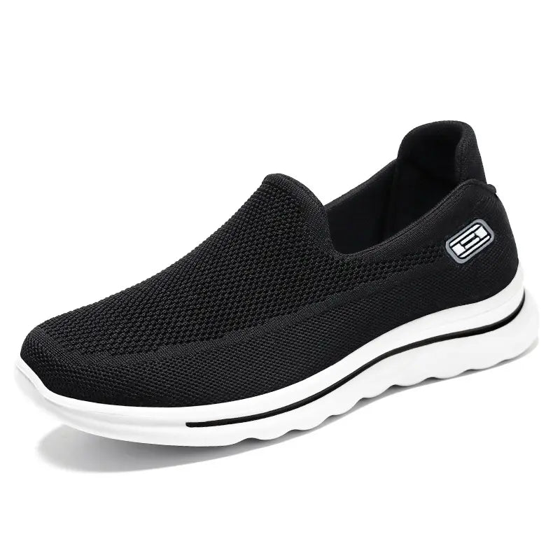 Black Veyla Comfort Knit Trainers slip-on sneaker with white EVA sole and a subtle side badge, shown from a three-quarter angle on a clean white background.