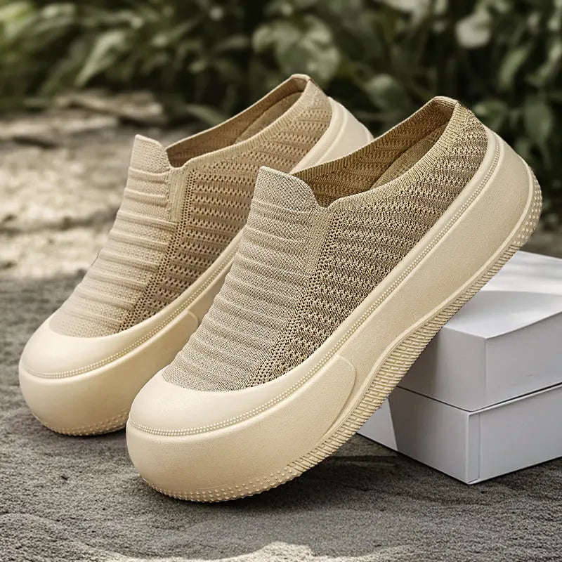 Pair of Vimera casual beige knit slip-on platform mules shown in a three-quarter view on a textured outdoor surface with greenery in the background. Features a round toe and thick, light-colored sole.