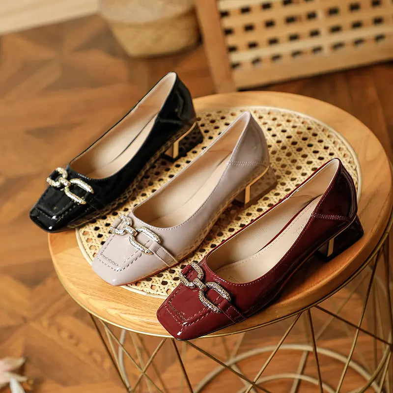 Vorlag women's patent leather pumps in black, taupe, and wine red, featuring square toes, gold-tone buckle embellishments, and block heels, displayed on a woven surface.