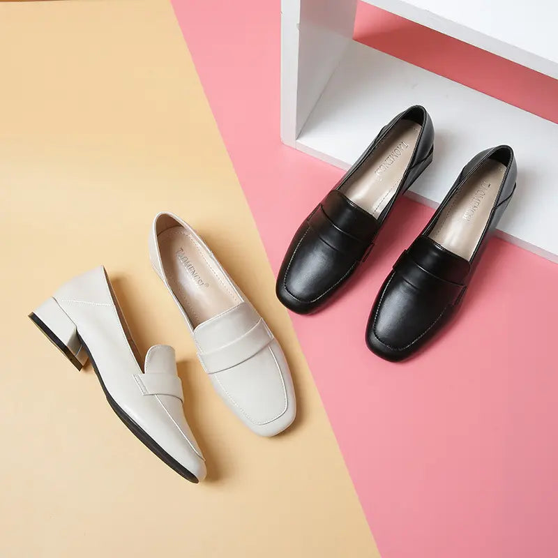 Studio arrangement of black and off-white Vylos square-toe loafers, showcasing their slip-on design, decorative vamp strap, and block heels on a split yellow and pink background.