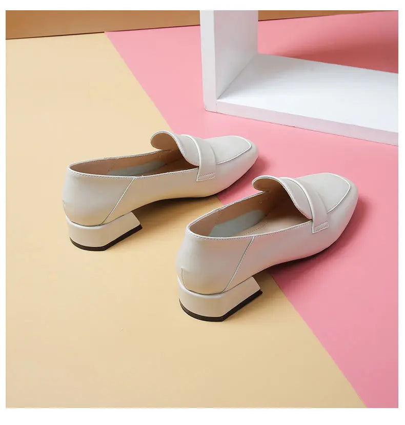 Off-white faux leather loafers with a square toe, decorative vamp strap, and a block heel, shown from a front-three-quarter angle on a pastel background.
