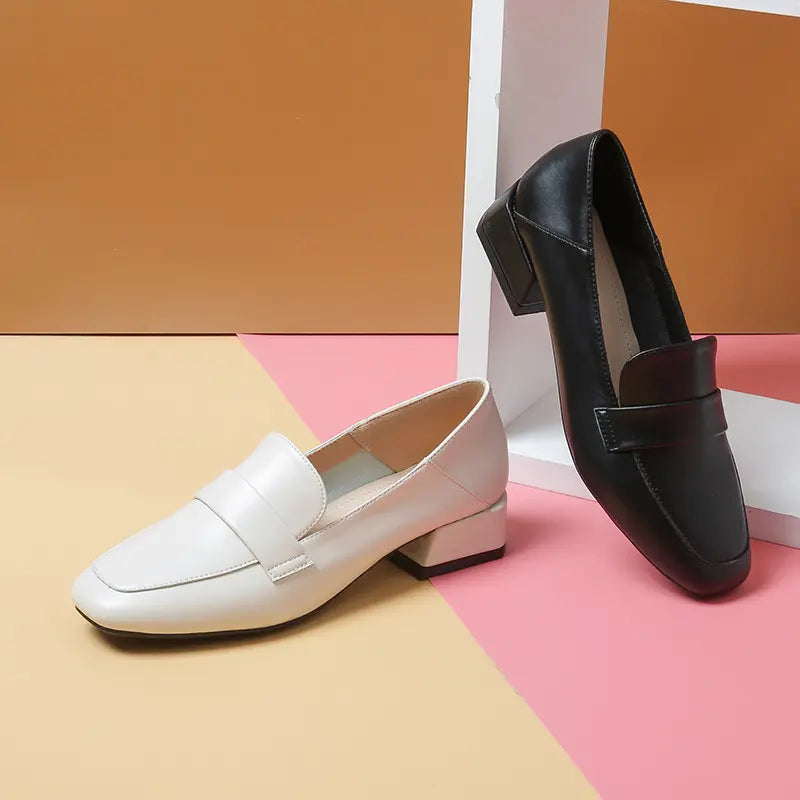 A pair of Vylos black and off-white square-toe loafers with block heels and decorative vamp straps, showcased side-by-side.