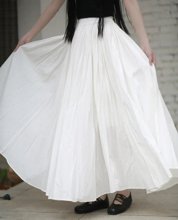 Woman wearing a voluminous white pure cotton maxi skirt with a gathered elastic waistband, showcasing its full A-line silhouette and flowing drape.
