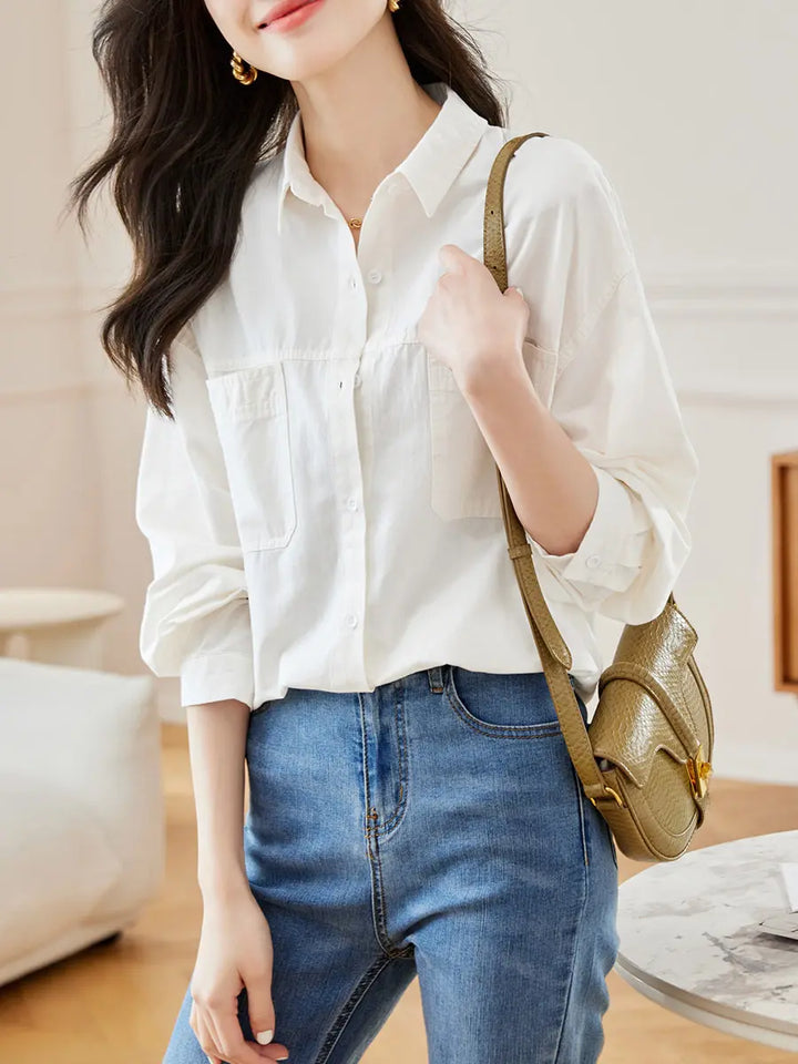 A woman wears a white long-sleeved relaxed-fit cotton shirt with a polo collar, paired with blue denim jeans and a green crossbody bag, showcasing casual everyday style.