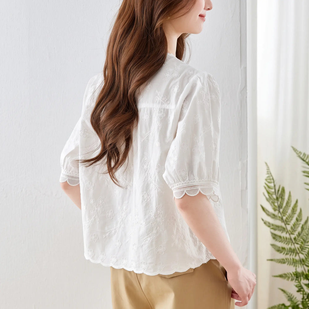 White cotton embroidered blouse with puff sleeves and scalloped lace trim, viewed from the back/side on a model.