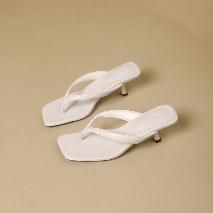 A pair of white heeled flip-flops with a sharp square toe and a slender stiletto heel, shown from a three-quarter angle on a neutral studio background.