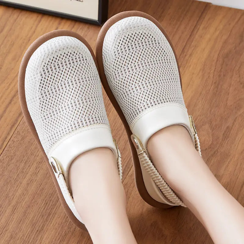 White breathable mesh slip-on mules shown worn on feet from a top-down view, featuring a rounded toe and flexible elasticated heel strap against a wooden floor background.