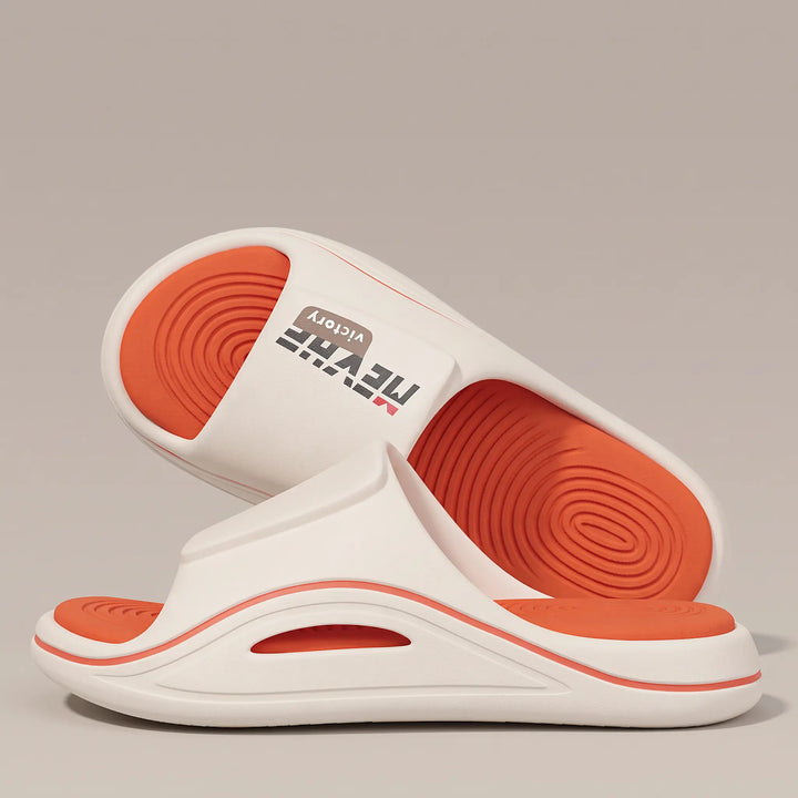 A pair of white and orange EVA slides with a thick sculpted sole and wave-textured footbed, shown from a three-quarter angle against a studio background.