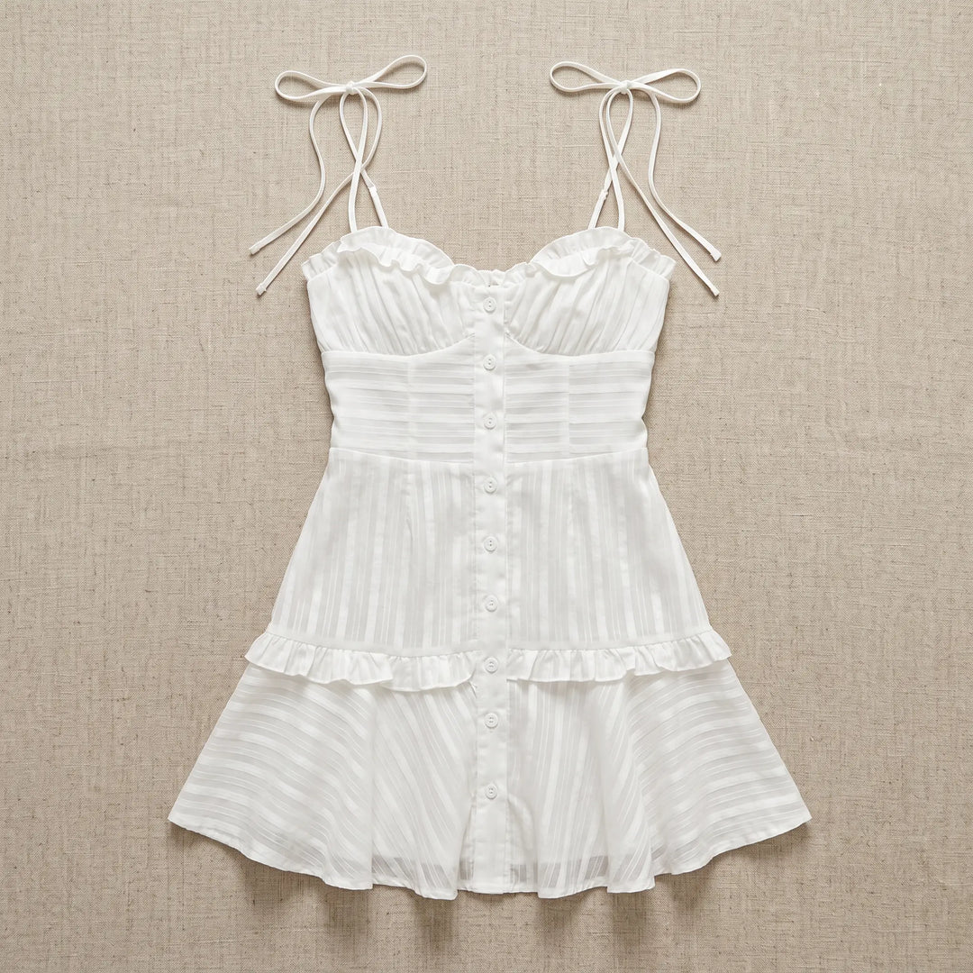 White sheer cotton voile mini dress with ruffled sweetheart neckline, adjustable spaghetti straps, and tiered ruffled skirt, shown flat lay.