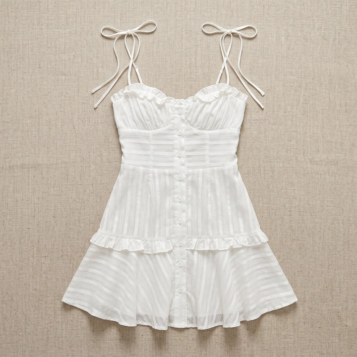 White sheer cotton voile mini dress with ruffled sweetheart neckline, adjustable spaghetti straps, and tiered ruffled skirt, shown flat lay.