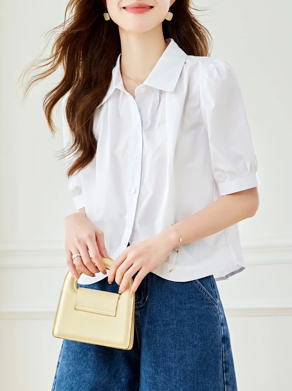Woman wearing a crisp white short-sleeve puff blouse with a pointed collar, paired with blue denim jeans and holding a small gold handbag.