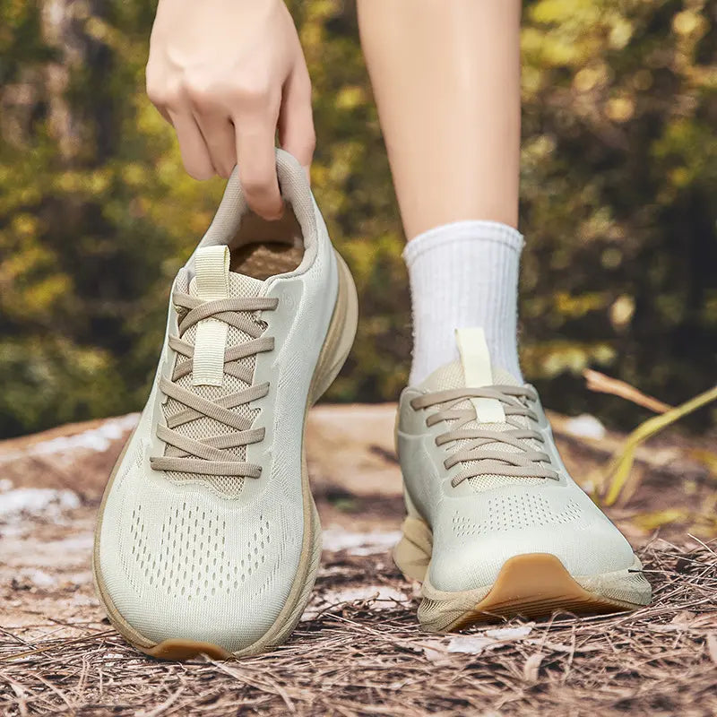 Close-up view of wide fit breathable athletic trainers in a light beige hue, worn with white socks in an outdoor natural setting.
