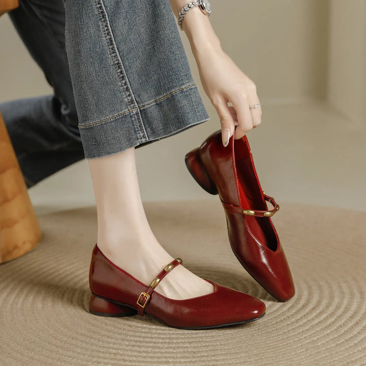 Wine red square toe Mary Jane shoes with a low block heel and a delicate gold-buckle strap, shown on a foot and held by hand.