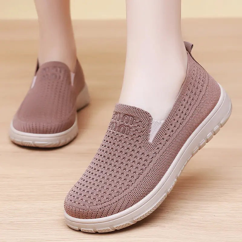 Close-up of women's breathable slip-on trainers in beige, worn on a foot, showcasing the textured flyknit mesh upper and cushioned sole.