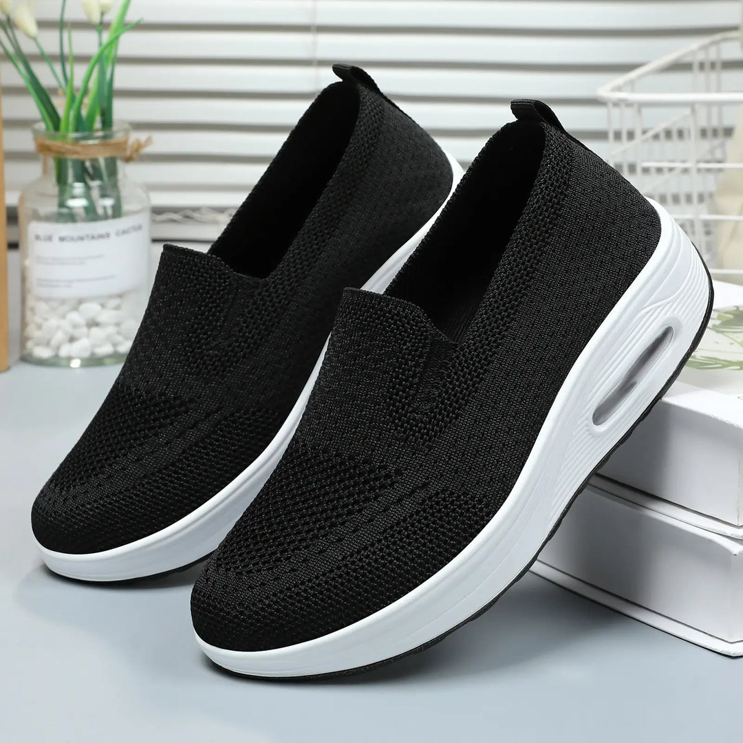 Pair of Xylos black breathable knit slip-on sneakers with white platform soles and visible air cushion heel.