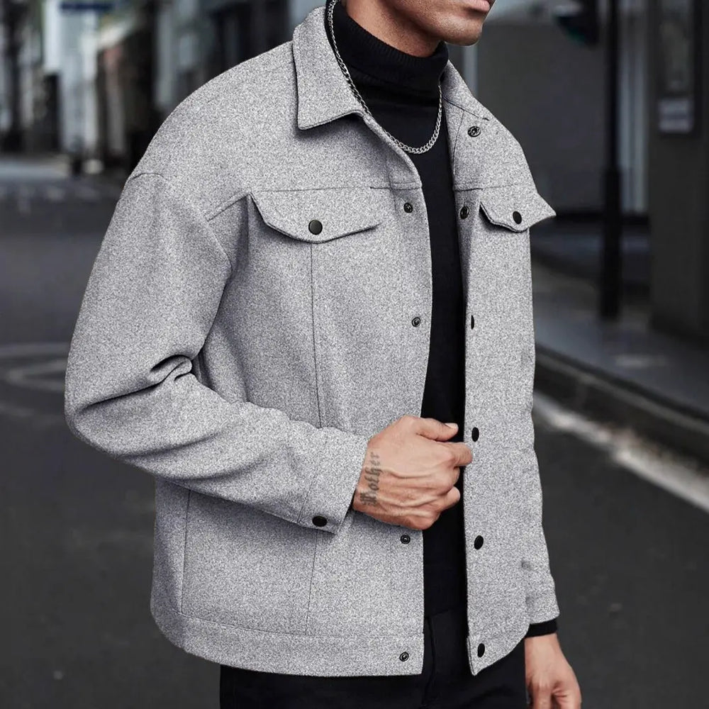 Men's Xylos textured casual jacket in heather grey, shown on a model in a three-quarter view with a black turtleneck and chain, set against an urban street background.