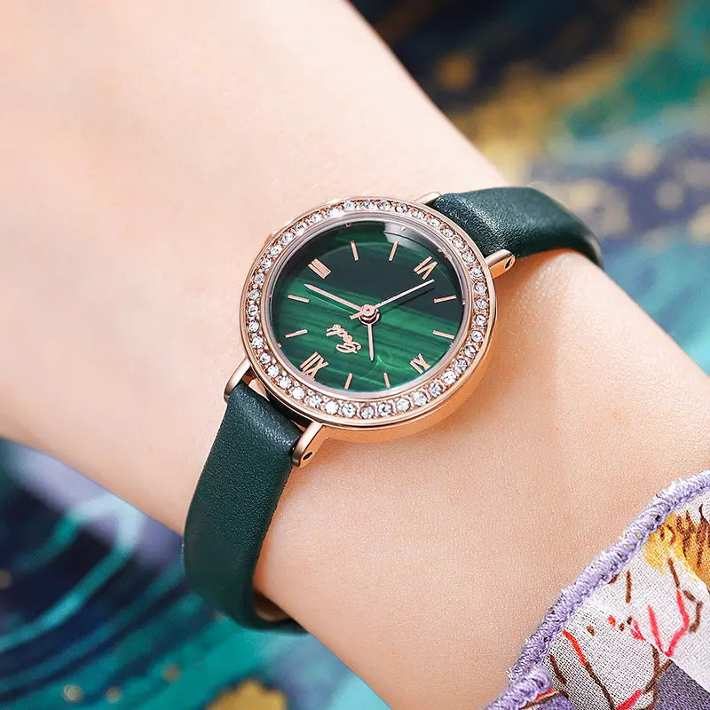 A Xylos rose gold watch with a captivating malachite dial and sparkling cubic zirconia bezel is worn on a wrist, showcasing its elegant design and dark green leather strap.