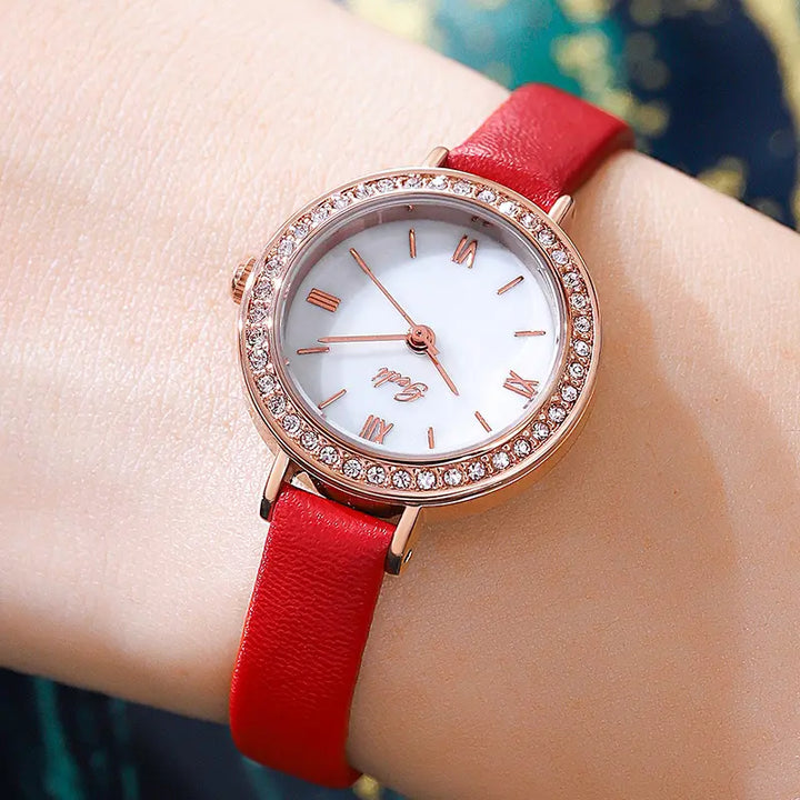Elegant Xylos rose gold ladies watch with a white analog dial, sparkling cubic zirconia bezel, and a vibrant red leather strap, shown on a wrist.