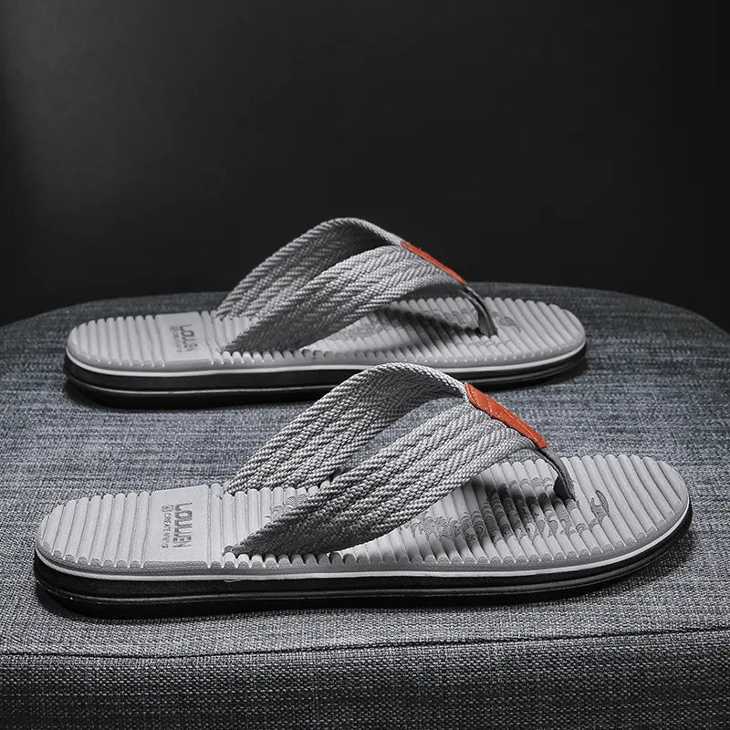 Men's Xyloza grey flip-flops with woven textile straps and a textured dark grey footbed, displayed from a three-quarter angle on a studio surface.