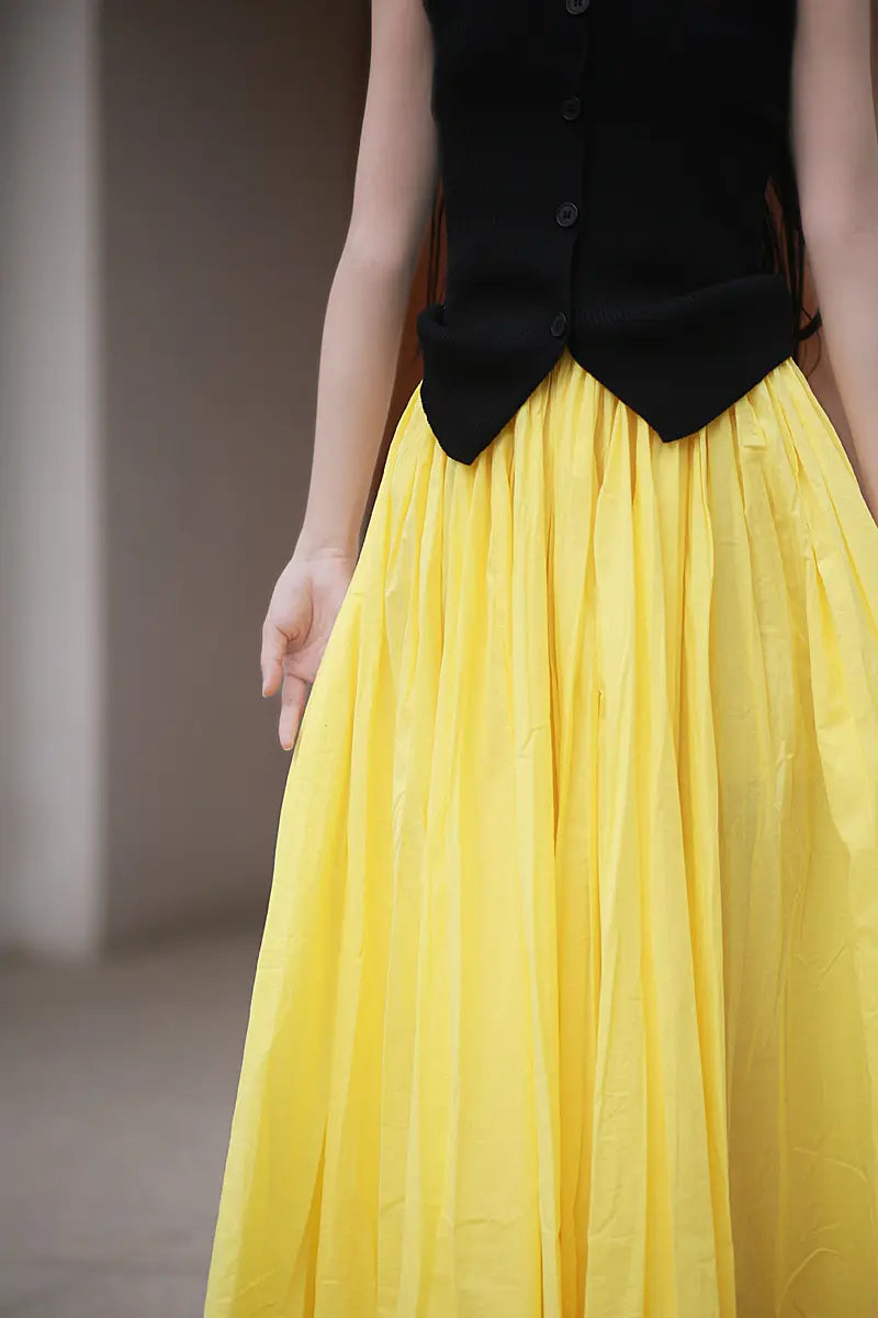 A woman models a voluminous yellow cotton maxi skirt with a black sleeveless top, showcasing the skirt&