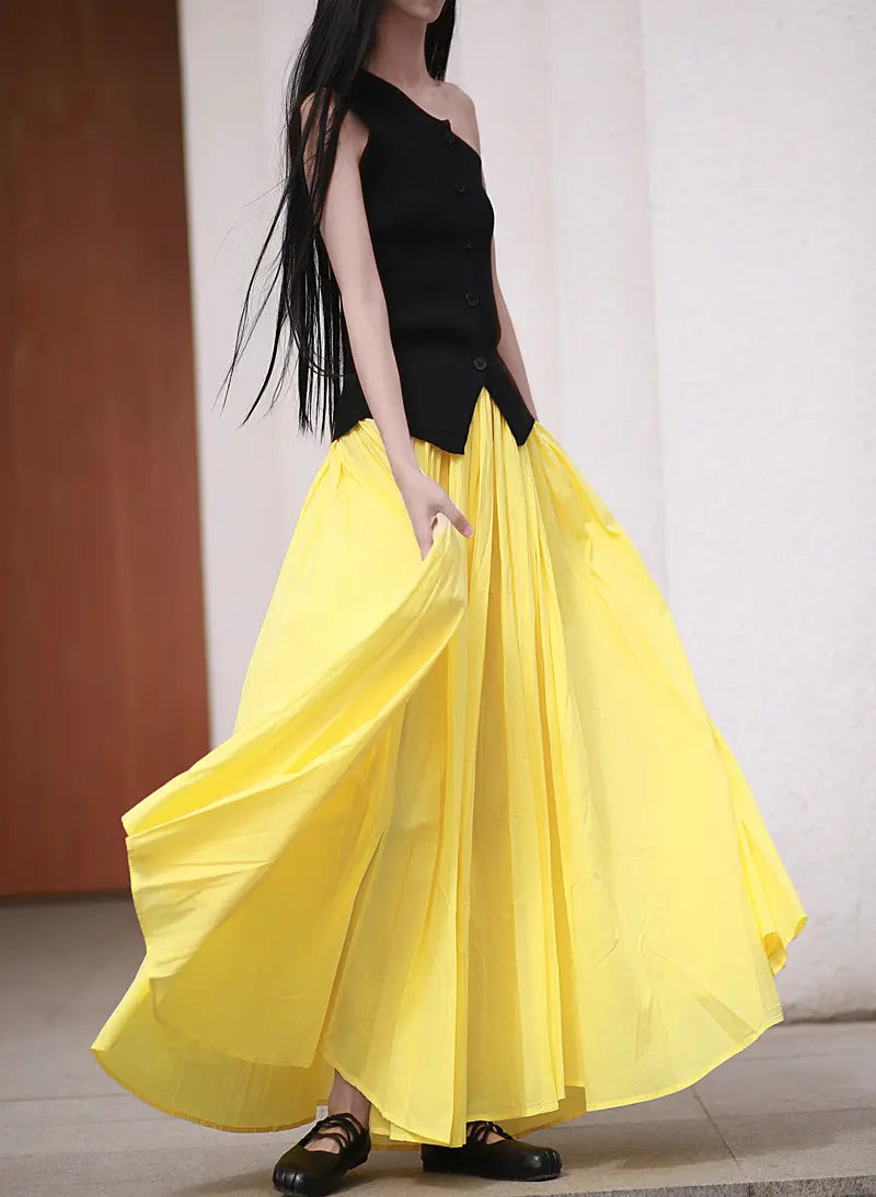 A woman models a voluminous yellow cotton maxi skirt with an elasticated waistband, showcasing its full, flowing silhouette and retro-inspired design.