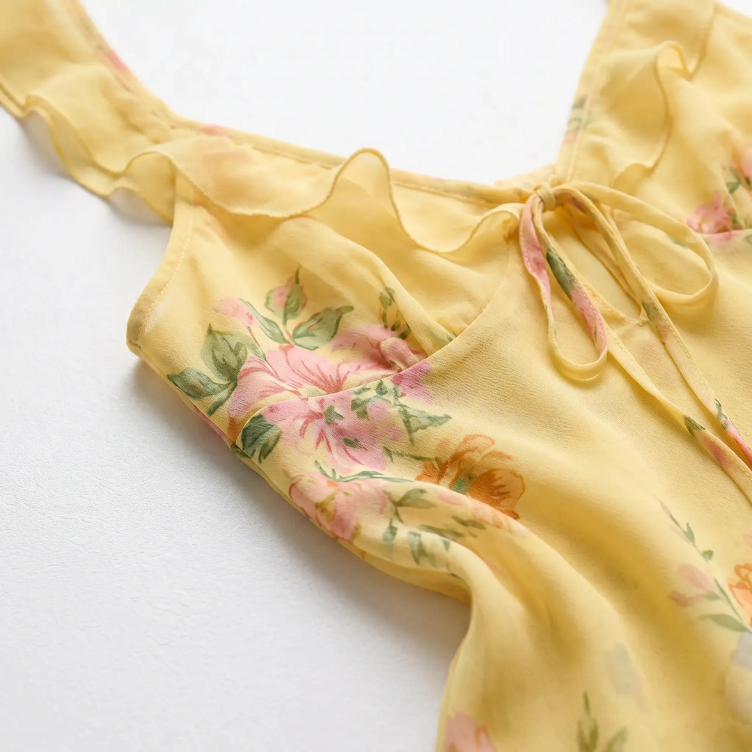 Close-up of a yellow sheer chiffon maxi dress featuring a plunging V-neck with delicate ruffles and an adjustable self-tie front, adorned with a soft floral print.