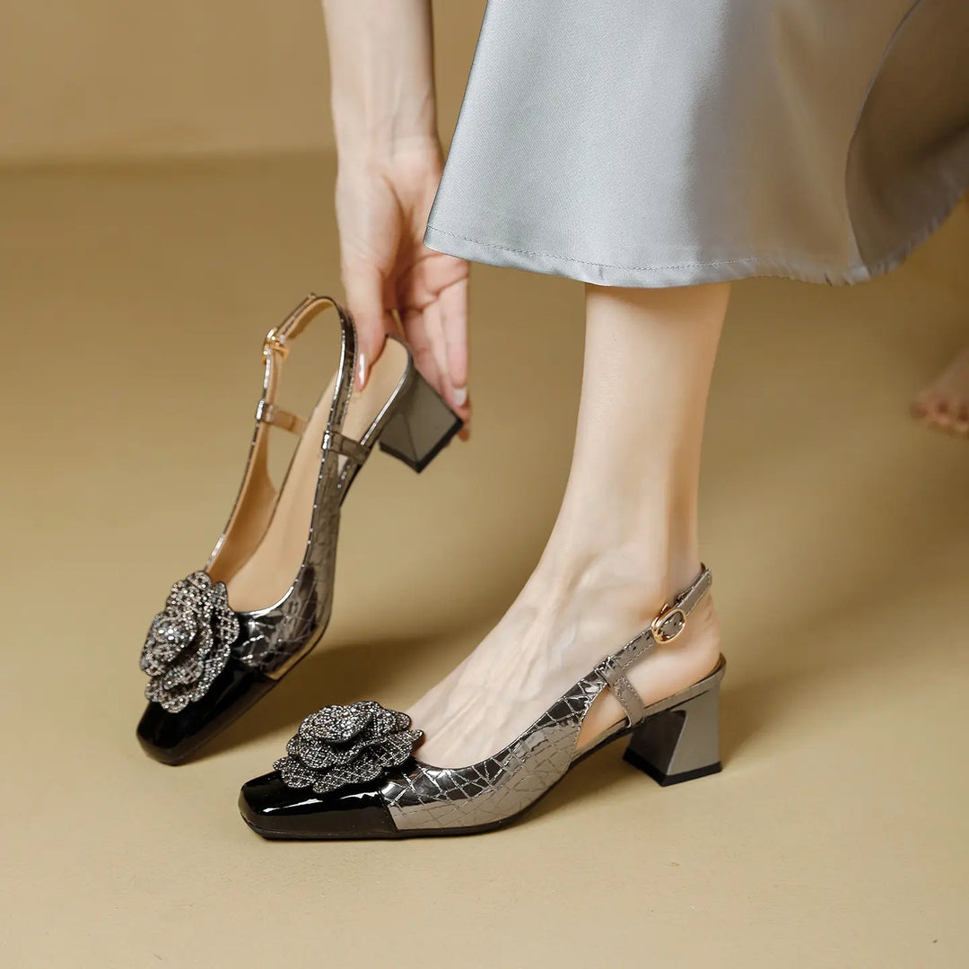 Elegant Zeloria slingback heels featuring a square toe, chunky block heel, and a dazzling jeweled floral embellishment on a metallic textured upper with a patent cap toe, shown on a model&