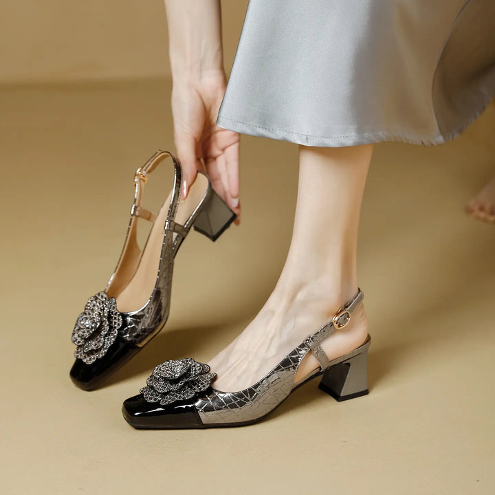 Elegant Zeloria slingback heels featuring a square toe, chunky block heel, and a dazzling jeweled floral embellishment on a metallic textured upper with a patent cap toe, shown on a model&