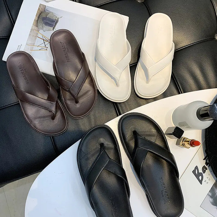 A flat lay arrangement featuring three pairs of Zenthel casual comfort sandals in dark chocolate brown, classic black, and crisp white, styled with lipstick and a perfume bottle.