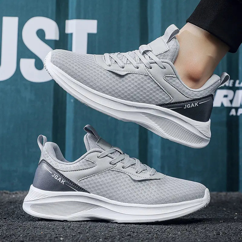 Pair of grey ZephyrStride men's casual sneakers, shown in a three-quarter view with one shoe on a foot and another below, featuring breathable mesh uppers and white layered soles.