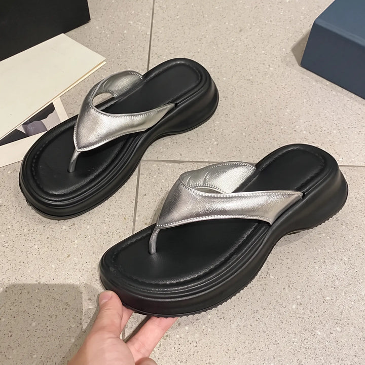 A pair of Zethel metallic silver platform thong sandals with a chunky matte black EVA sole, shown from a three-quarter angle on a tiled studio floor.