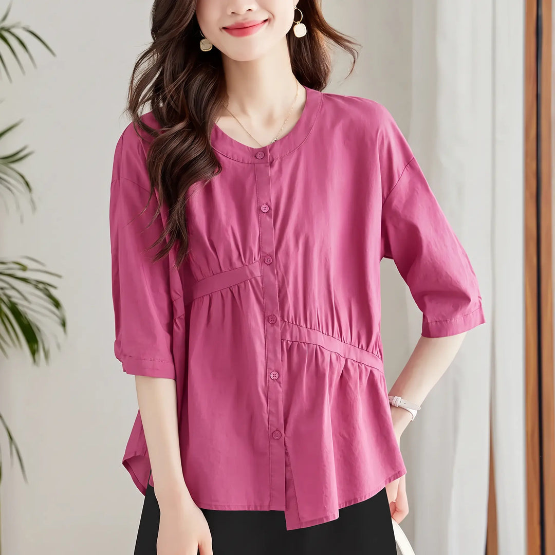 Chic women's asymmetric peplum blouse in deep rose purple, featuring diagonal front pleating, round neckline, 7/8 sleeves, and tonal button front closure, worn by a model.