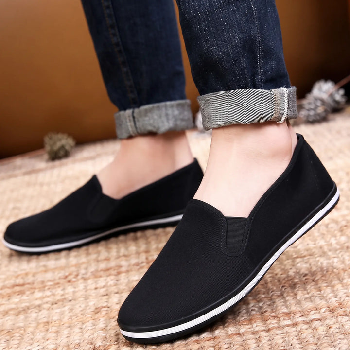 Black canvas slip-on loafers worn by a person, showcasing their breathable, lightweight comfort and casual style with a white stripe detail on the rubber sole. These Zydana shoes are ideal for everyday wear.