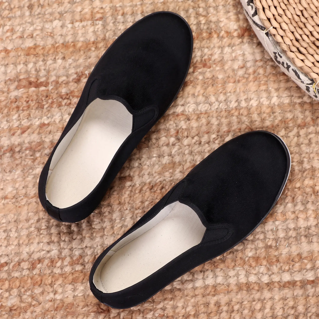 Pair of Zydana black canvas loafers with white interior lining and black rubber soles, viewed from a top-down angle on a textured rug.