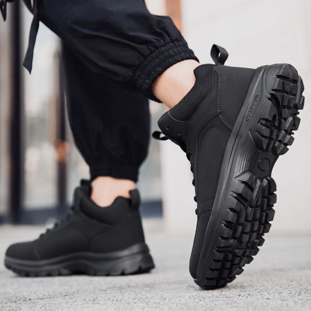 Black mid-top winter boots worn by a person, showcasing the durable sole and ankle support, with &