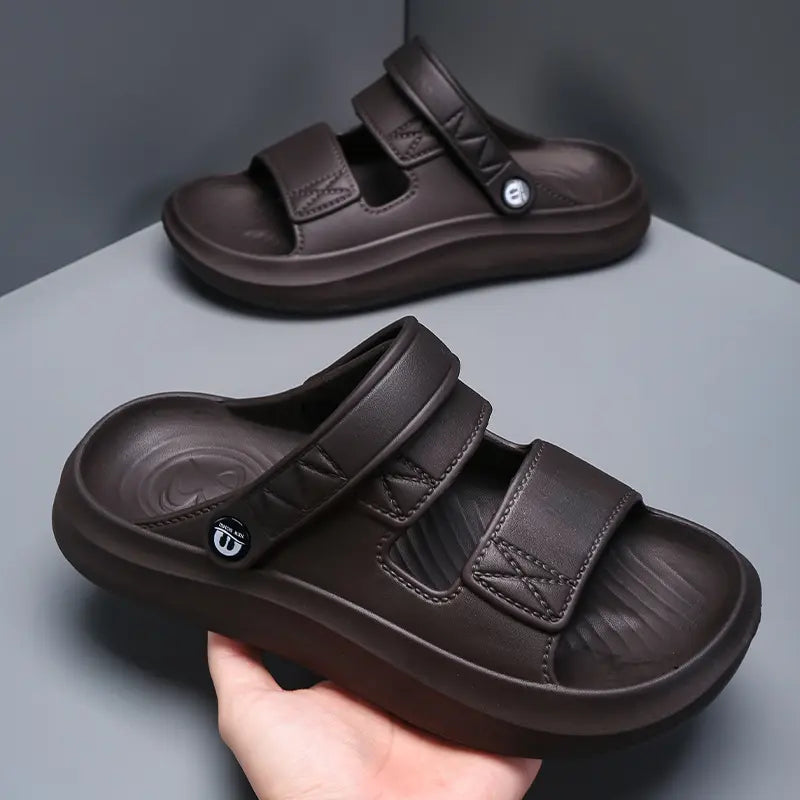 Dark brown men's Zykos EVA sandals with dual adjustable velcro straps, shown in a three-quarter view held by a hand, highlighting the contoured footbed and thick lug sole.