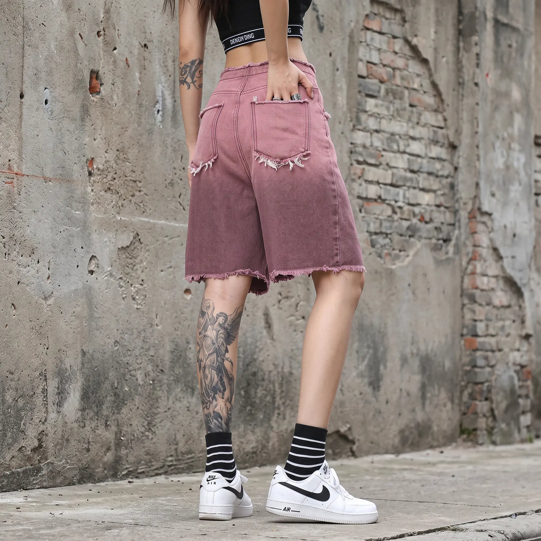 Zykra wide-leg denim shorts in an ombré gradient wash from brown to dusty rose, featuring a frayed distressed hem and graphic print on the leg, shown from a three-quarter back view.