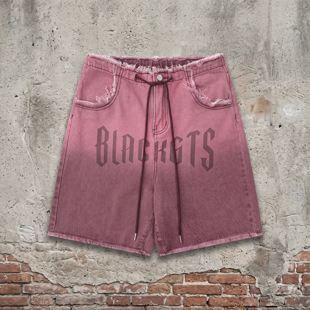Zykra wide leg distressed denim shorts in an ombré wash from brown to dusty rose, featuring a frayed hem and a prominent 'BLACKGTS' graphic print on the leg.