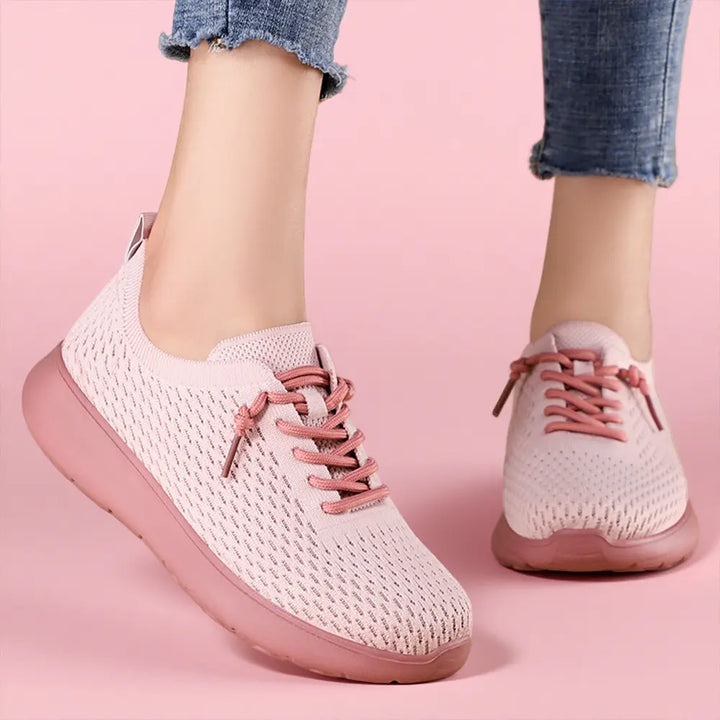 Dusty rose breathable knit trainers with pink laces worn by a person, showcasing the seamless upper and cushioned sole in a lifestyle context against a pastel pink background.